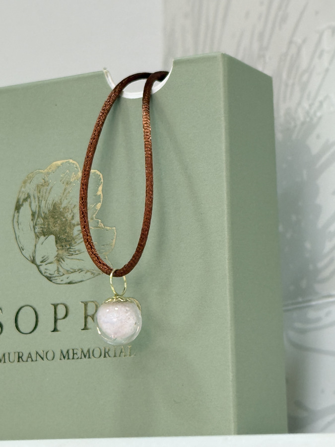 Pingente memorial da Sopro com acabamento dourado sobre cordão marrom